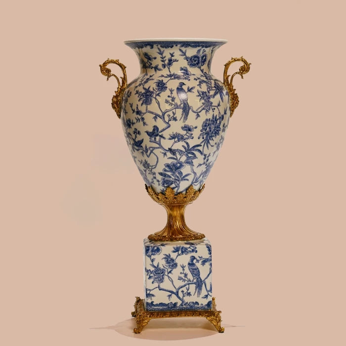 Detailed view of decorative vase's square brass base with floral repoussé and blue-white ceramic patterns.