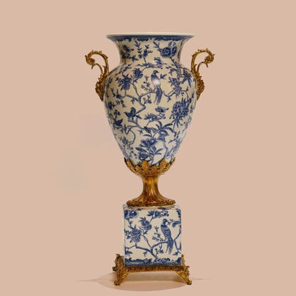 Detailed view of decorative vase's square brass base with floral repoussé and blue-white ceramic patterns.