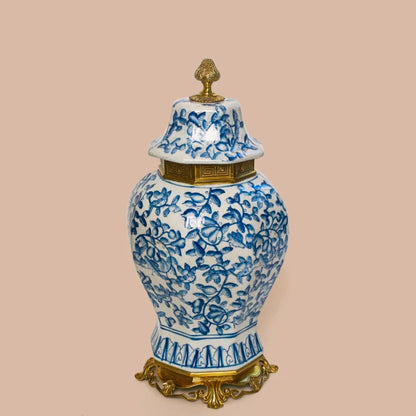 Close-up detail of a blue floral pattern and ornate brass base on a white ceramic jar.