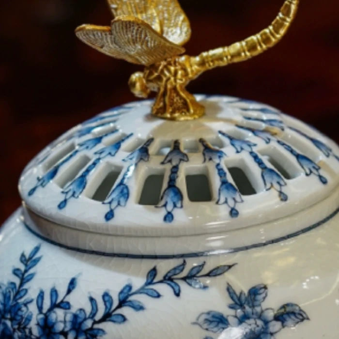 Detailed shot of gilded brass dragonfly perched on aroma stove lid with blue motifs