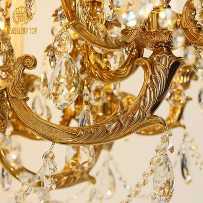 Close-up of gold brass chandelier arm showing intricate vine carvings and hanging crystal droplets under warm light.